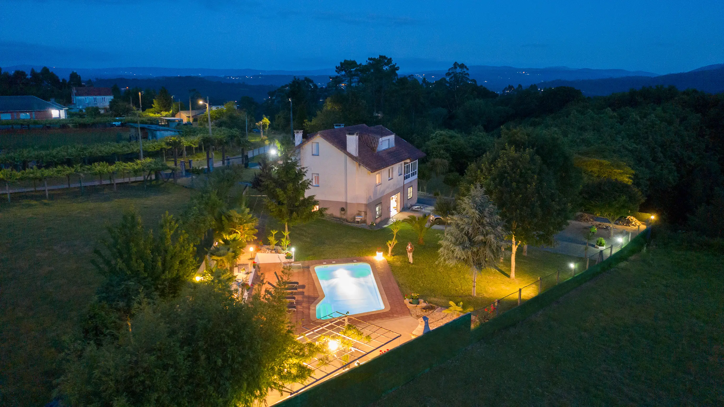 Casa rural de noche con luces cálidas en ventanas y jardín