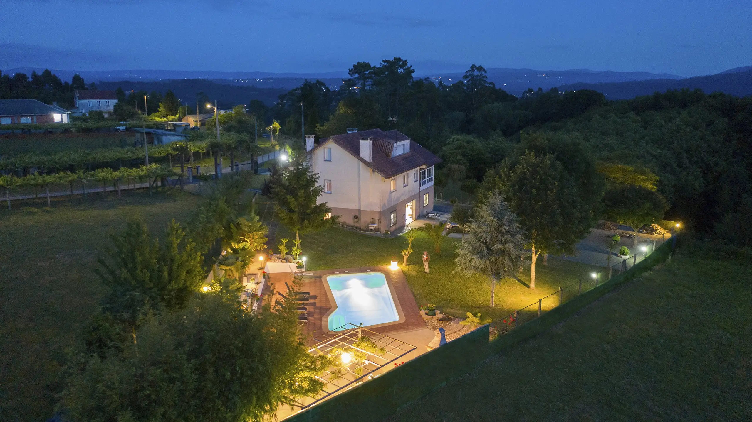 Casa rural de noche con luces cálidas en ventanas y jardín